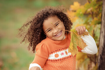 Cute afro girl smiling broadly outdoors and enjoying autumn day in park.