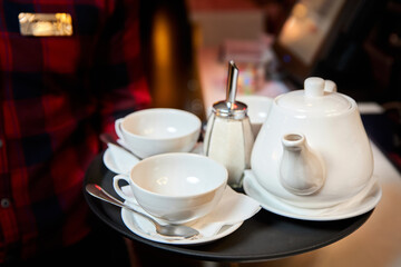 The waiter holds in his hand a tray with a kettle, tea cups and sugar. Close-up, selective focus.