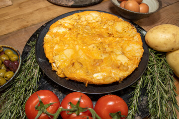 A delicious Spanish tortilla on a wooden kitchen table surrounded by the ingredients used to create the dish