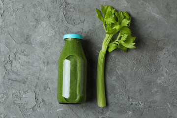 Bottle of green smoothie and celery on gray background