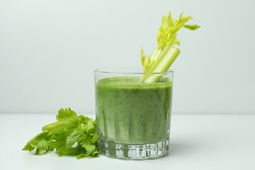 Glass of green smoothie with сelery on white table