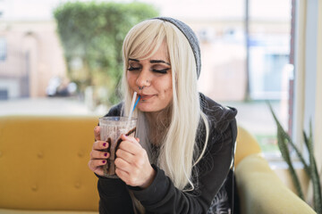 Cute young Spanish woman with blond hair and piercings enjoying her drink