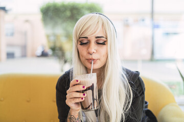 Cute young Spanish woman with blond hair and piercings enjoying her drink