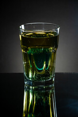 Premade setup for saint patrick drink. Shot glass of blue curacao drink inside the light gold beer. Reflecting surface and dark gradient background