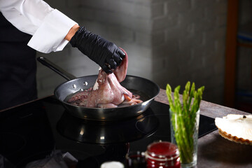 Cook puts the octopus in the pan. Cooking octopus. Seafood dishes. Protein food. An unrecognizable person. Dark background.