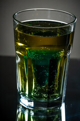 Premade setup for saint patrick drink. Shot glass of blue curacao drink inside the light gold beer. Reflecting surface and dark gradient background