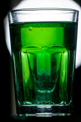 Premade setup for saint patrick drink. Shot glass of blue curacao drink inside the light gold beer. Reflecting surface and sharp front light in the background