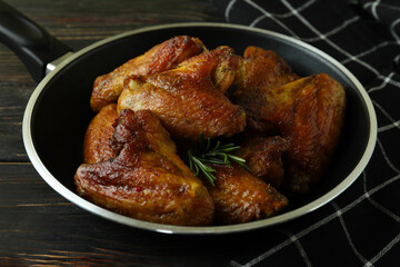 Pan with baked chicken wings and kitchen towel on wooden background