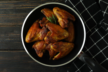 Pan with baked chicken wings and kitchen towel on wooden background