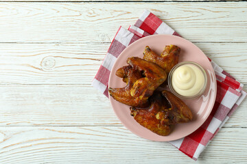 Plate with baked chicken wings and sauce on kitchen towel on wooden background