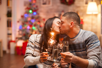Happy boyfriend kissing girlfriend while holding hand fireworks on christmas.
