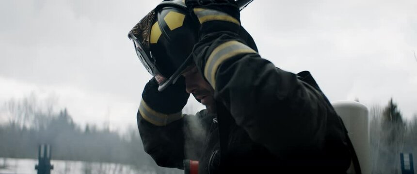 Hero shot portrait of American Caucasian male firefighter taking off his protective helmet, looking into camera. Shot with 2x anamorphic lens 100 FPS slow motion