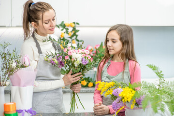 Fototapeta na wymiar Woman teaches to young girl arranging flower at floral shop