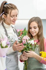 Young woman teaches to young girl arranging flower at flower shop