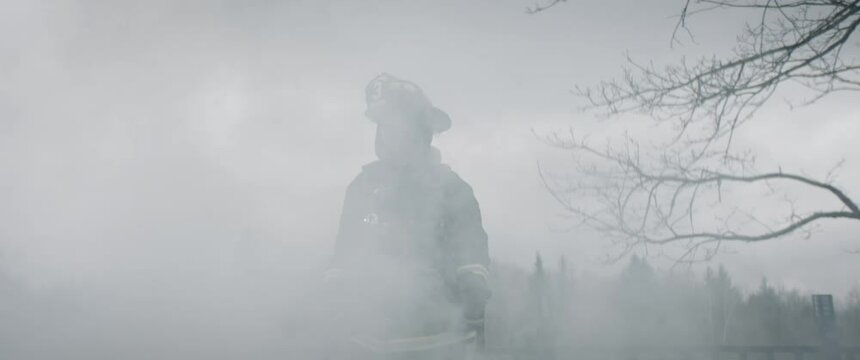 Silhouette of American female firefighter in traditional helmet and full gear standing in the smoke. Shot with 2x anamorphic lens. 100 FPS slow motion
