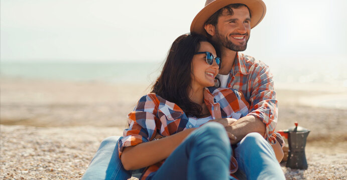 happy romantic couple sits on sea beach, talks, laughs and hugs. moments of love