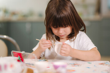 Adorable little girl during printing easter eggs at home. Beauutiful girl preparing for easter at home during quarantine. Self isolated