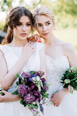 two girls in wedding dresses with bouquets on a background of flowers