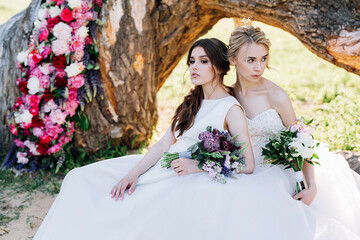 two brides with bouquets are sitting on the background of a decorated tree