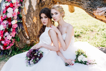 two brides with bouquets are sitting on the background of a decorated tree