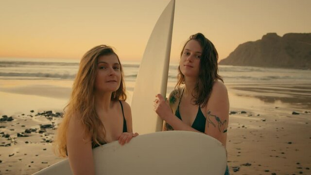 Portrait of two female surfers stand on sand beach at popular surfing spot location. Look at camera, authentic and candid real people. Young professional women surfers. Millennial sports lifestyle