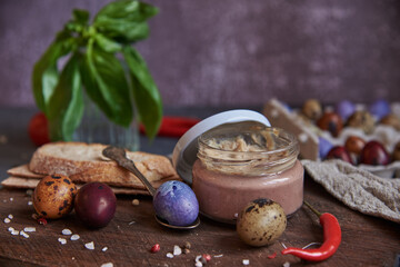 Meat pate in a glass jar on a cutting board and painted quail eggs. Easter background, meat delicacies.