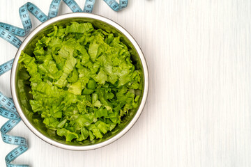 Salad with fitness measuring tape over wooden background
