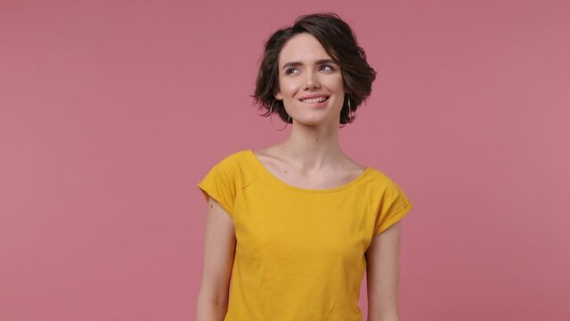 Brunette short hairdo young woman 20s wears basic casual yellow t-shirt looking around think dream put hand prop up on chin isolated on pastel pink background studio portrait People lifestyle concept