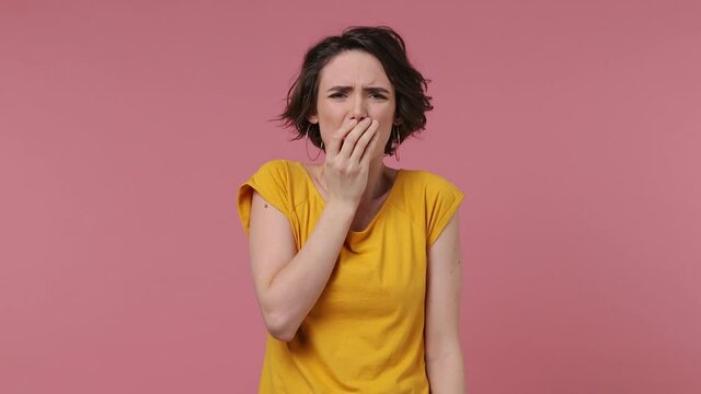 Scared shocked short hairdo young woman 20s wears basic casual yellow t-shirt looking camera covering hiding face with hands isolated on pastel pink background studio People emotions lifestyle concept