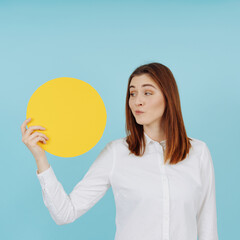 Dubious young woman looking at a yellow circle in her hand