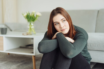 Naklejka premium Thoughtful young woman sitting on the floor in the living room