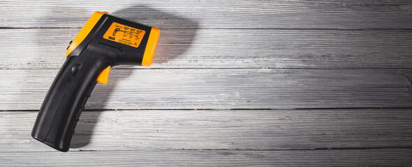 Yellow-black pyrometer on a wooden background. A device for non-contact temperature measurement. © bearok