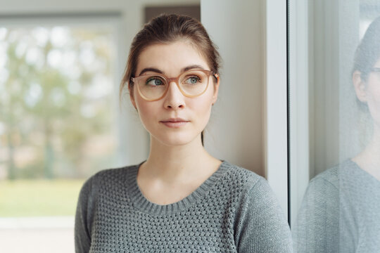 Attractive young woman wearing eyeglasses looking aside through a window
