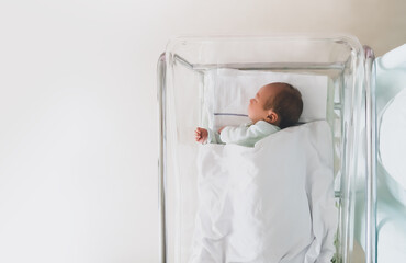 Newborn baby is sleeping in small transparent portable plastic bed. Baby first days of life is...
