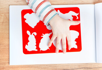 Children's hand holds a stencil on the background of the sketchbook. Early baby development concept.