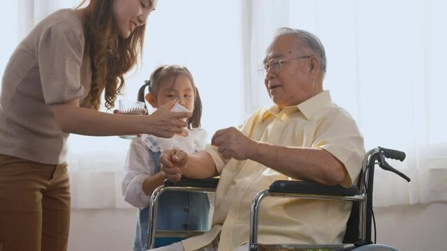 Asian elderly person sitting in a wheelchair, sick with granddaughter and daughter walking, bring father medicine and water time to eat, family visit to support old senior man
