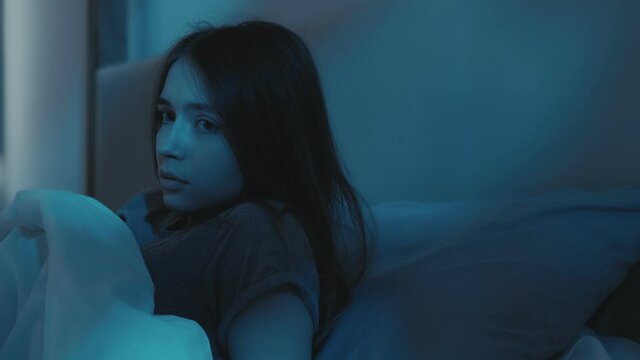 Bed nightmare. Sleep disorder. Bad dream. Panic attack anxiety. Disturbed scared girl woke up opened eyes late at night in dark home bedroom with blue moonlight.