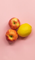 On a pink background in the center are two ripe apples and one yellow lemon