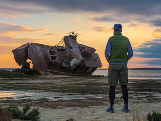 A man stands on the shores of the Aral Sea by an old abandoned ship. Kazakhstan. The ship was cut...