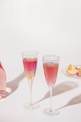 Bottle of rose champagne sparkling wine and beatiful bright glasses with sunlight on light table