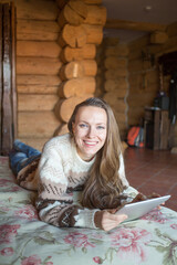 Fototapeta premium Rural escape. Woman in wooden rural scenery home interior, woman lying on bed with a laptop