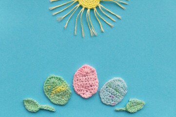 On a aquamarine background is a composition of crocheted products. Imitation of a easter day. Sun and eggs.