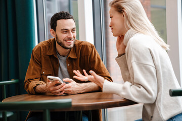 Happy young couple talking while sitting in cafe indoors