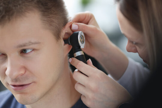 Otorhinolaryngologist examining ear of sick man with otoscope closeup