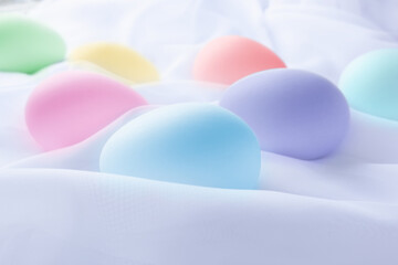 Easter eggs in pastel colors laying on heavenly white silky sheets, pink, blue, purple