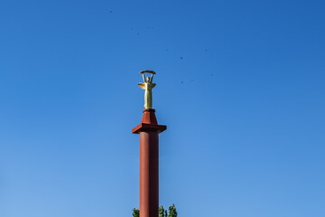 Kherson, Ukraine - July 22, 2020: Top of Victory Monument with a statue of Greek goddess Nike (Kherson) isolated on a blue sky background, close-up. Tall pillar topped with a female figure with wings