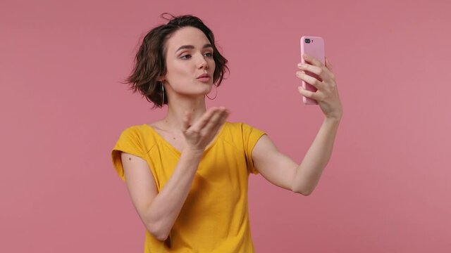 Pretty brunette short hairdo young woman 20s wears basic casual yellow t-shirt posing doing selfie shot on mobile phone post photo on social network isolated on pastel pink background studio portrait