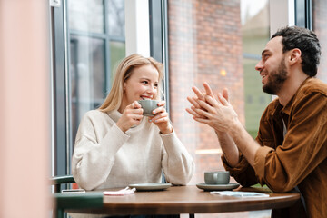 Young man and woman smiling and talking while drinking coffee in cafe