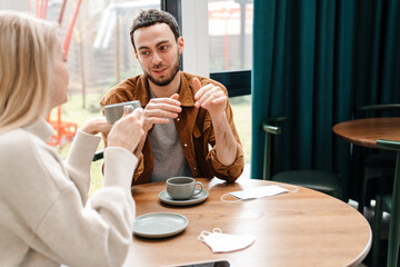 Young man and woman smiling and talking while drinking coffee in cafe