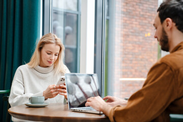 Focused man and woman using laptop and cellphone while drinking coffee